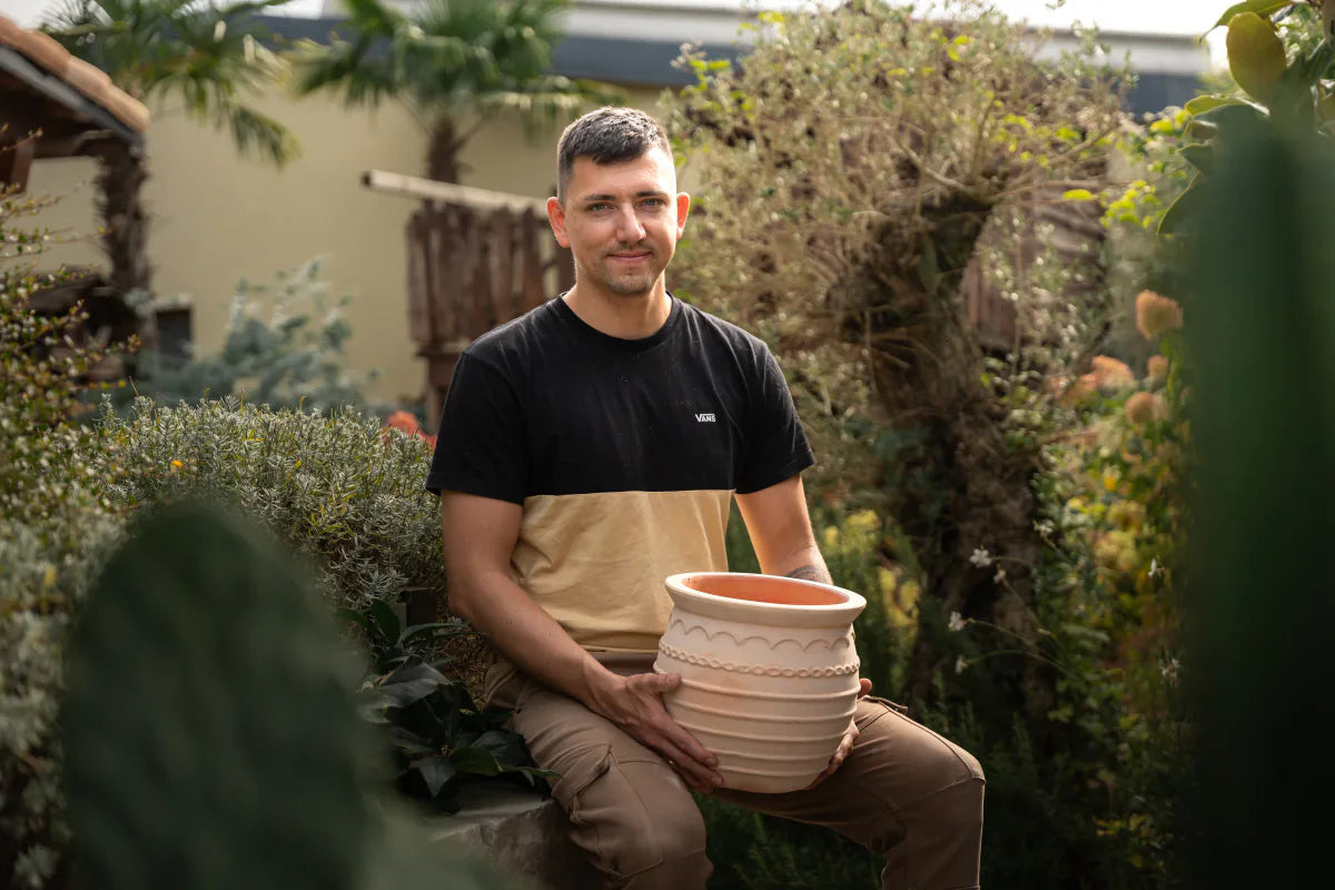 Pablo sitzt im Garten und hält einen Terrakottatopf
